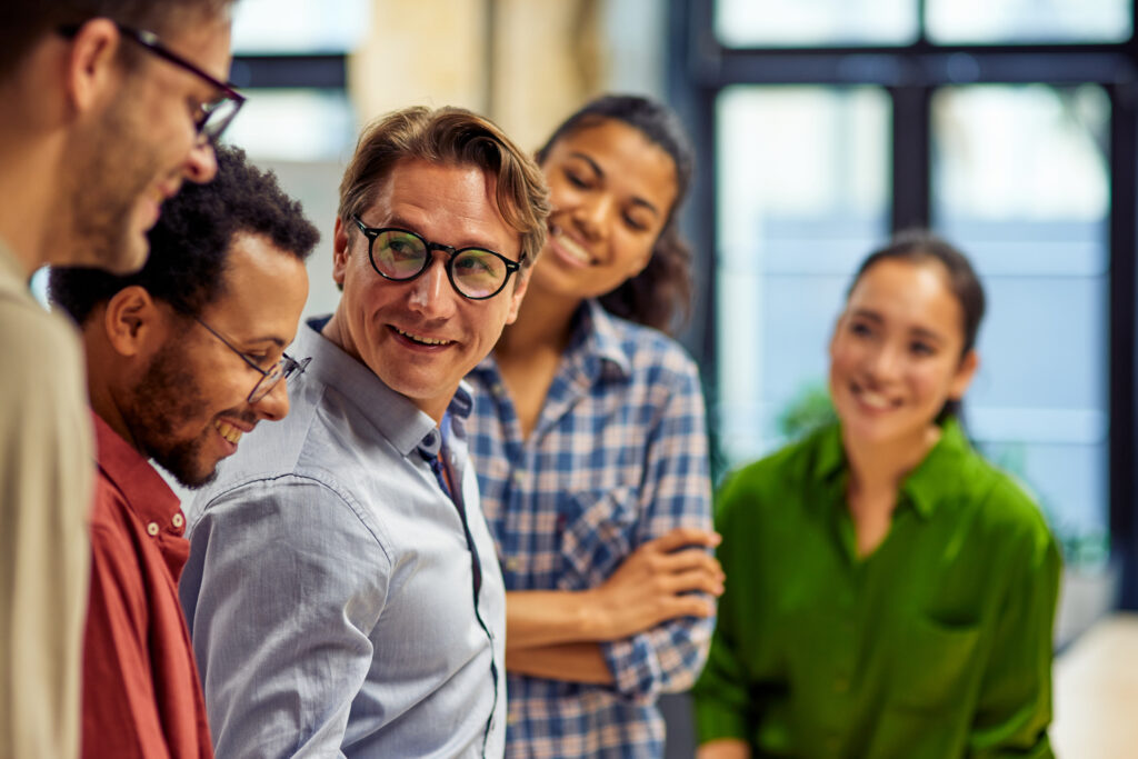 Confident businessman discussing project results and sharing ideas with young motivated multi ethnic team while standing together in the modern office